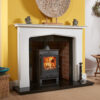 Marble fire surround in white fitted on a yellow wall, accompanied with a granite hearth and a wood burning stove.